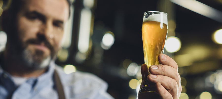 Brewer inspecting a freshly poured beer in a clean glass, highlighting the importance of tank hygiene and beerstone removal with rotating spray nozzles.